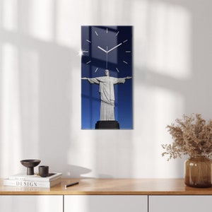 May include: A clock with a white face and black hands is superimposed over a photograph of the Christ the Redeemer statue in Rio de Janeiro, Brazil. The statue is white and stands against a blue sky.