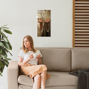 Puede incluir: Una obra de arte mural rectangular que representa una figura religiosa con las manos extendidas. La obra de arte presenta una paleta de colores neutros con tonos de marrón y beige. La imagen está montada en una pared blanca.