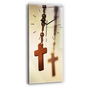 Puede incluir: Una cruz de madera cuelga de una cadena de rosario con cuentas delante de una esfera de reloj. La cruz es marrón y las cuentas son marrón oscuro. La esfera del reloj es blanca con agujas negras y números negros.