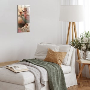 Puede incluir: Una pintura de dos ángeles con alas, uno con un vestido rosa y el otro con un vestido azul, flotando sobre una mujer dormida en una cama blanca. La pintura está enmarcada y colgada en una pared blanca.