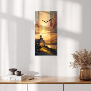 May include: A clock with a church and a lake in the background. The church is lit by the sun, which is setting behind the clouds. The clock face is black with white numbers and hands.
