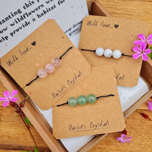 May include: Three handmade bracelets with different colored beads on brown card stock with the text "Daisies Crystals" and "With love..." on each card. The bracelets are made with pink, white, and green beads.