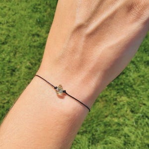 May include: A simple black string bracelet with a clear teardrop-shaped crystal charm.