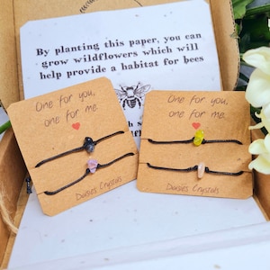 May include: Two sets of friendship bracelets with the text "One for you, one for me." Each set has two bracelets with different colored crystals. The bracelets are on a brown card with the text "Daisies Crystals".