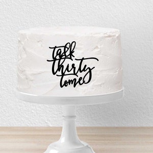 Op de afbeelding: Witte cake met zwarte frosting en de woorden "Talk Thirty To Me" erop geschreven.