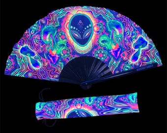 May include: A black folding fan with a psychedelic design featuring an alien face, mushrooms, and swirling patterns in neon pink, green, and blue colors. The fan is closed and has a black handle with the text "ROCKET MERCH" printed on it. The fan comes with a matching carrying case.