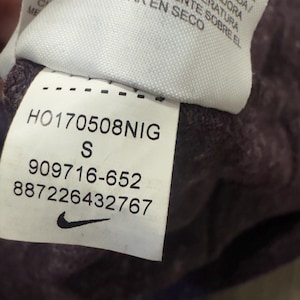 K&ouml;nnte beinhalten: Nahaufnahme eines Etiketts mit dem Nike-Logo und Produktinformationen. Das Etikett zeigt den Text "HO170508NIG", die Gr&ouml;&szlig;e "S" und die Nummern "909716-652" und "887226432767". Das Etikett ist wei&szlig; mit schwarzem Text.