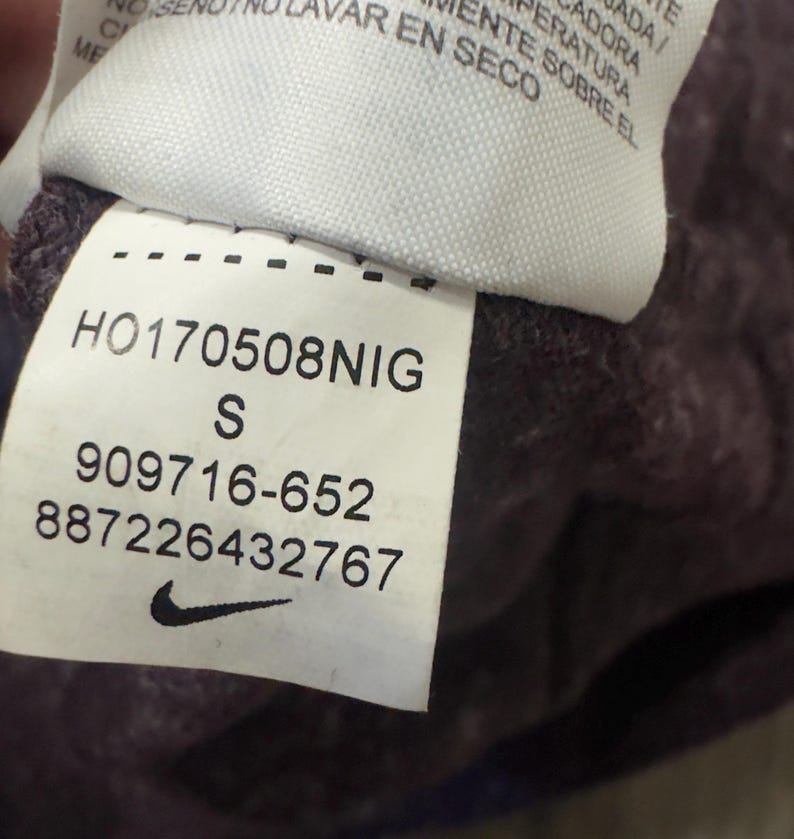 K&ouml;nnte beinhalten: Nahaufnahme eines Etiketts mit dem Nike-Logo und Produktinformationen. Das Etikett zeigt den Text "HO170508NIG", die Gr&ouml;&szlig;e "S" und die Nummern "909716-652" und "887226432767". Das Etikett ist wei&szlig; mit schwarzem Text.