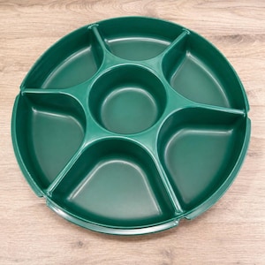 May include: A dark green, round serving tray with six compartments. The tray is divided into sections of varying sizes, with a central circular well. The tray is made of a smooth, solid material and is designed for serving snacks or appetizers.