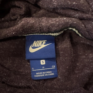 K&ouml;nnte beinhalten: Nahaufnahme eines dunkelvioletten Hoodies mit einem kleinen wei&szlig;en Fleckenmuster. Ein blaues Etikett mit dem Nike-Logo und dem Text "S P CH" ist sichtbar. Auf dem Etikett steht auch "MADE IN CHINA" und "FABRIQU&Eacute; EN CHINE".