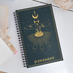 Diário de cartas de tarô do julgamento com um caderno espiral em branco de tarô dourado e azul com estética bruxa