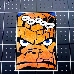 May include: A comic book illustration of The Thing from the Fantastic Four. He is orange and rocky with a stern expression. He has a thought bubble above his head that says "Keep out of my way!"