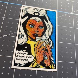 Puede incluir: Una ilustraci&oacute;n de c&oacute;mic de una mujer con cabello blanco y un atuendo azul y amarillo. Ella sostiene un vaso de agua y una burbuja de pensamiento sobre su cabeza dice "No soy mandona, soy la jefa".