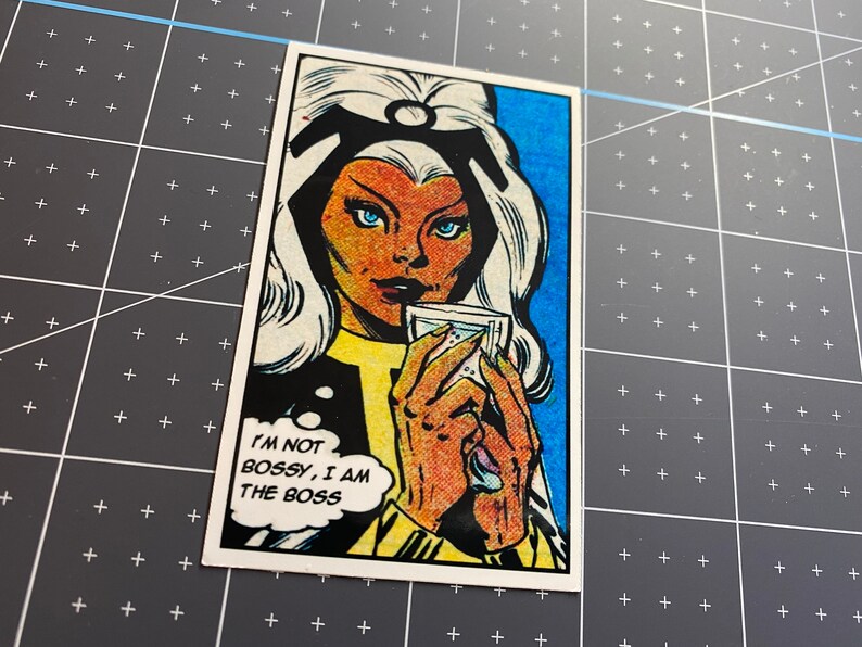 Puede incluir: Una ilustraci&oacute;n de c&oacute;mic de una mujer con cabello blanco y un atuendo azul y amarillo. Ella sostiene un vaso de agua y una burbuja de pensamiento sobre su cabeza dice "No soy mandona, soy la jefa".