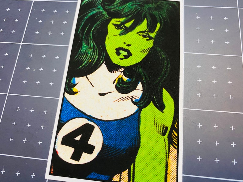 Pu&ograve; includere: Un'illustrazione di fumetto verde e blu di una supereroina con lunghi capelli verdi. La supereroina indossa un costume blu e bianco con un grande numero "4" sul petto.
