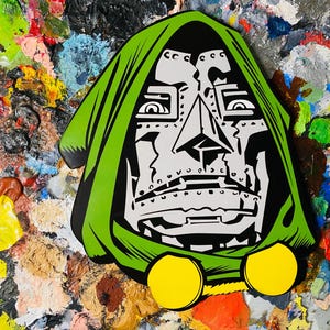 May include: A graphic illustration of Doctor Doom, featuring a green hood, a silver face, and yellow accents. The artwork is set against a colorful background of mixed paint. The design is bold and stylized, with sharp lines and a comic book aesthetic.