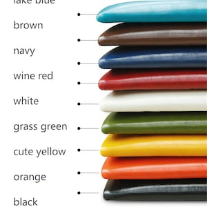 Puede incluir: Una pila de diez cojines de imitación de cuero de colores en varios colores, incluyendo azul lago, marrón, azul marino, rojo vino, blanco, verde hierba, amarillo bonito, naranja y negro.