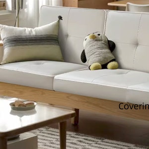 May include: A white leather sofa with a wooden frame and a plush penguin toy. The sofa has two cushions and a striped throw pillow. The sofa is labelled "Coveringart".