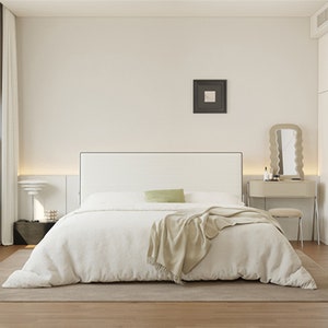 Puede incluir: Un dormitorio blanco con una cama grande, una cabecera blanca y una manta blanca. Hay una mesa pequeña con un espejo y un taburete al lado de la cama. Las paredes son blancas y el suelo es de madera.