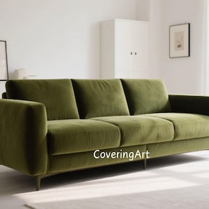 May include: Olive green velvet sofa with three seat cushions and a low profile. The sofa has a modern design with a rectangular shape and thin, dark legs. The text "CoveringArt" is visible on the front.