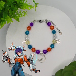 May include: A colorful beaded bracelet with purple, orange, blue, and yellow beads. The bracelet has silver star charms and a crescent moon charm. The bracelet is on a white surface.