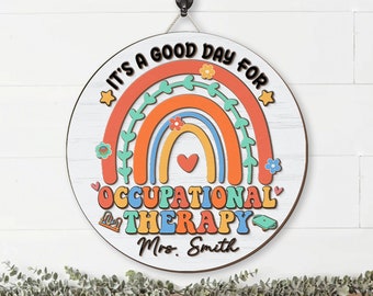May include: A round wooden sign with a rainbow design and the text "It's a good day for Occupational Therapy Mrs. Smith".