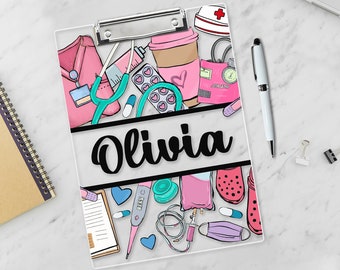 May include: A pink and white clipboard with a personalized name "Olivia" in black cursive font. The clipboard is decorated with a variety of medical illustrations, including a stethoscope, a syringe, a thermometer, and a bandage.