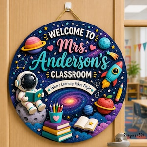 May include: A circular wooden classroom sign with a dark blue space background featuring the text "WELCOME TO Mrs. Anderson's CLASSROOM" and "Where Learning Takes Flight". It includes a 3D astronaut, rocket, planets, books, and pencils.