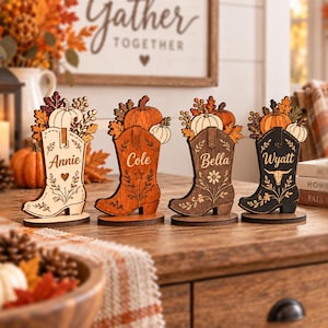 May include: Four wooden cowboy boot ornaments featuring autumn-themed cutouts of pumpkins and leaves. Each boot is personalized with the names Annie, Cole, Bella, and Wyatt, and decorated with engraved floral, star, heart, or bull skull motifs.