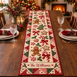 May include: A rectangular quilted table runner featuring a cream-colored center panel with gingerbread men, candy canes, stars, and red bows. The border consists of red, green, and white geometric patterns. The text The Williams is printed at the bottom.