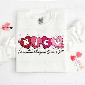 May include: White t-shirt with a pink and red graphic of the word "NICU" in hearts with a baby bottle and a pacifier. The text "Neonatal Intensive Care Unit" is below the graphic.