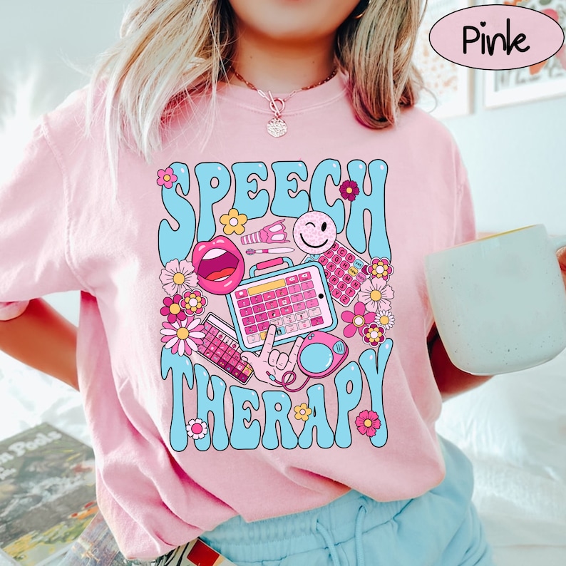 May include: Pink t-shirt featuring a graphic design of speech therapy tools in a retro style. The design includes a speech bubble, a mouth, a keyboard, a microphone, and flowers. The text "Speech Therapy" is written in a retro font.