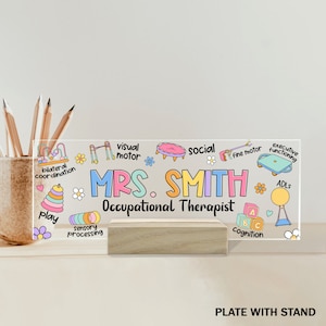 May include: A clear acrylic desk plate with a stand, featuring a colorful illustration of various occupational therapy tools and the text "MRS. SMITH Occupational Therapist".