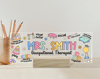 May include: A clear acrylic desk plate with a stand, featuring a colorful illustration of various occupational therapy tools and the text "MRS. SMITH Occupational Therapist".