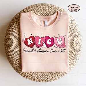 May include: A pink t-shirt with the words "NICU" spelled out in pink hearts with a baby bottle and a duck graphic. The text "Neonatal Intensive Care Unit" is below the hearts.