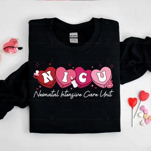 May include: Black t-shirt with a graphic of the word "NICU" spelled out in pink and red hearts. The hearts have a baby bottle, a pacifier, and a duck inside. The text "Neonatal Intensive Care Unit" is below the hearts.