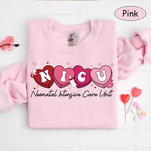 May include: Pink sweatshirt with a graphic of the word "NICU" spelled out in pink hearts with a baby bottle and a pacifier inside each heart. The text "Neonatal Intensive Care Unit" is printed below the hearts.