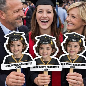 Pu&ograve; includere: Una celebrazione di laurea con tre sagome di un bambino con cappello e toga, ognuna con il nome "Olivia" e il testo "LOOK WHO'S GRADUATED -2026-". Una laureata con cappello e toga sorride, circondata dalla sua famiglia.