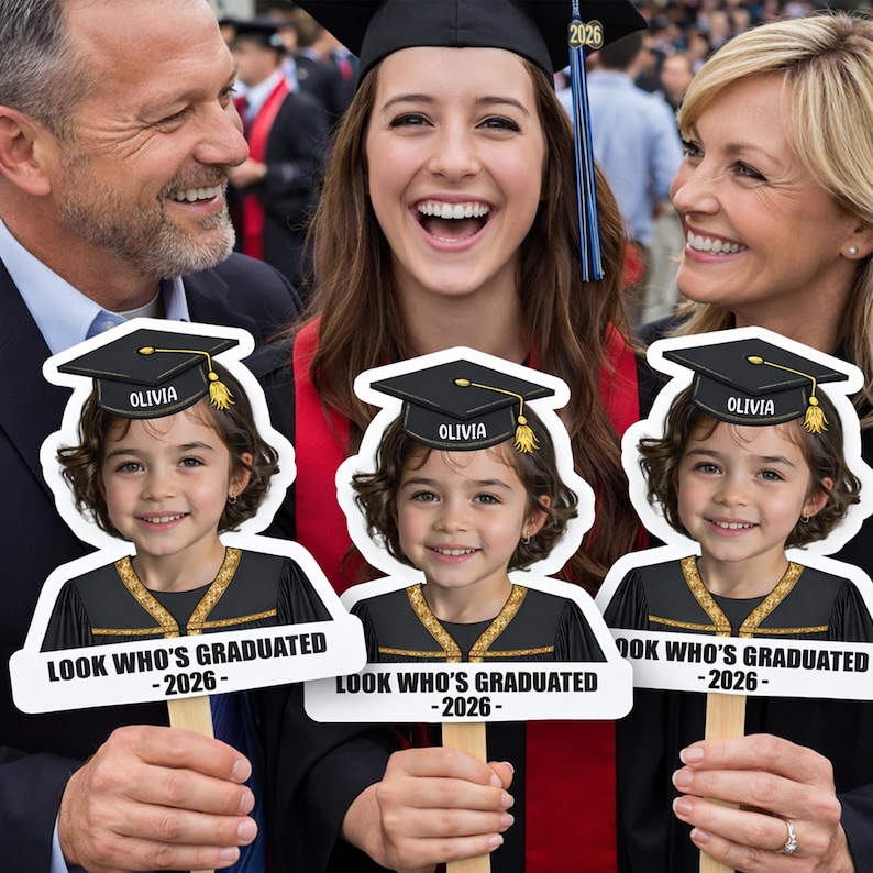 Pu&ograve; includere: Una celebrazione di laurea con tre sagome di un bambino con cappello e toga, ognuna con il nome "Olivia" e il testo "LOOK WHO'S GRADUATED -2026-". Una laureata con cappello e toga sorride, circondata dalla sua famiglia.