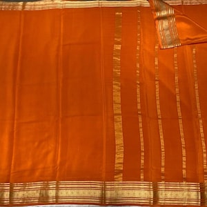 May include: A vibrant orange fabric featuring horizontal gold metallic borders at the top and bottom edges, complemented by vertical gold metallic stripes running along the right side of the textile surface.
