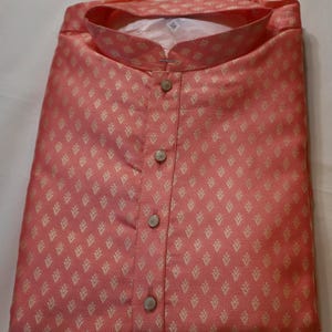 May include: A coral-colored long-sleeve shirt featuring a repeating gold-toned leaf pattern. The shirt has a mandarin collar, a front button placket with four visible buttons, and a white interior tag clearly displaying the number 38.