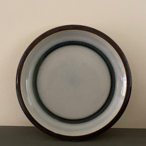 May include: A white ceramic plate with a brown rim and blue and white concentric circles.