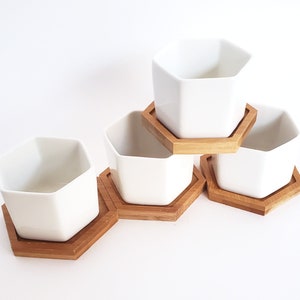 May include: Set of four white hexagonal ceramic planters with matching wooden hexagonal bases. The planters are stacked in a pyramid shape.