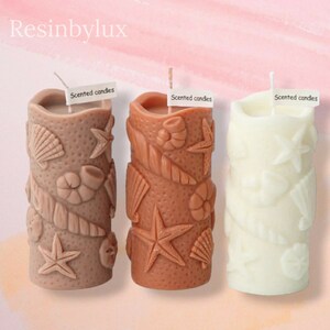 May include: Three scented candles with a beach theme. The candles are decorated with seashells, starfish, and other ocean-inspired designs. The candles are in brown, beige, and white.