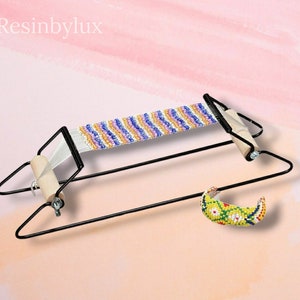 Peut inclure: Un métier à tisser en métal noir avec des bobines en bois pour tisser des bracelets en perles. Un bracelet en perles fini est présenté dans le coin inférieur droit de l'image.