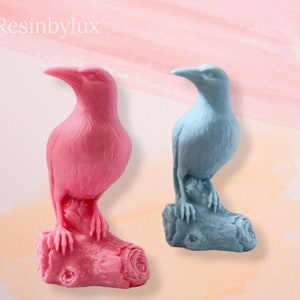 May include: Two resin bird figurines perched on tree branches. The bird on the left is pink and the bird on the right is light blue.