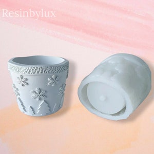May include: Two white resin molds for making candles or planters. The smaller mold is shaped like a pot with a snowflake and tree design. The larger mold is a cylinder with a flat bottom.