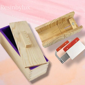 May include: A wooden soap mould kit with a silicone mould, a wooden cutting guide, and a stainless steel soap cutter. The silicone mould is purple and has a wooden lid. The cutting guide has a ruler marked with numbers 1 to 5. The soap cutter has red handles.