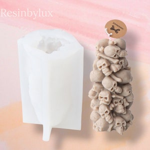 May include: White silicone mold for making a skull candle. The mold is shaped like a tall, thin tower. The candle is made of a light brown wax and is decorated with skulls and bones. The candle is labeled "Handmade".