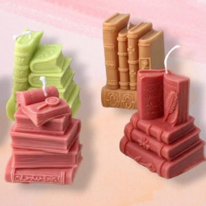 Può includere: Cinque candele decorative a forma di libro in vari colori e design. Le candele sono impilate in diverse configurazioni, alcune con dettagli intricati e altre con un design più semplice.